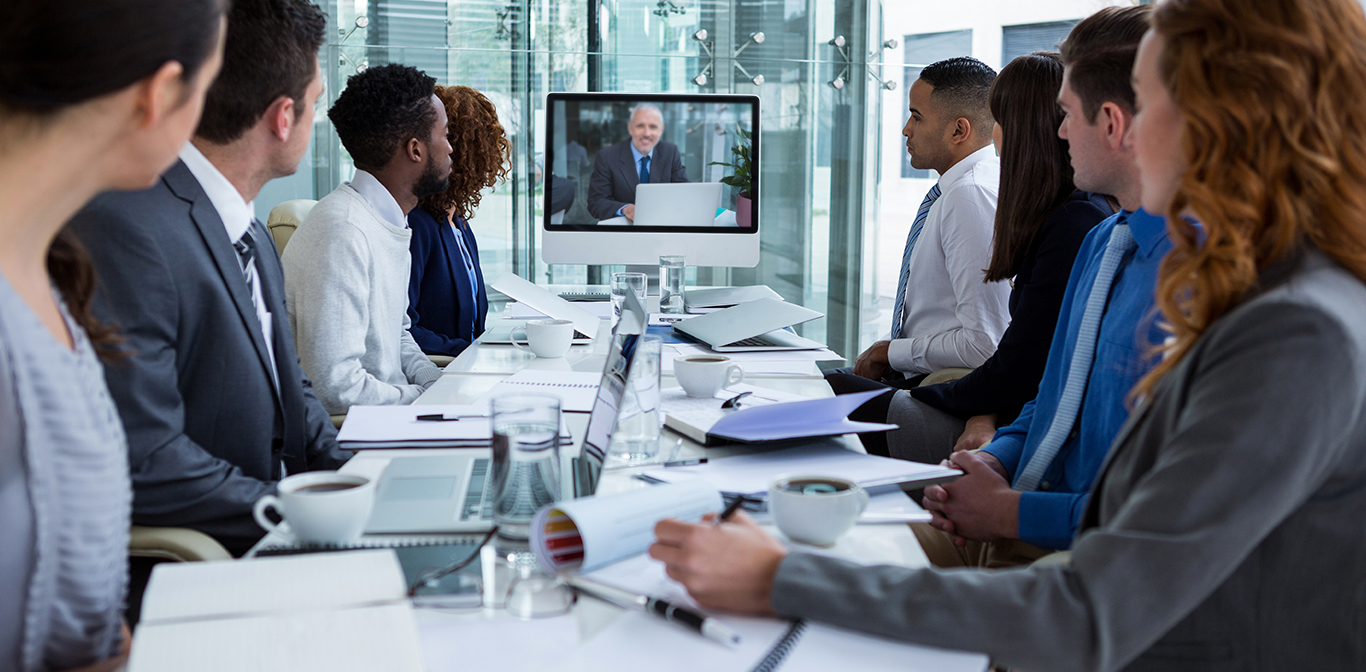 Eight professionals sitting at a table and looking at a screen with a man with a laptop