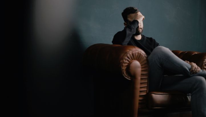 Man sitting on couch with his hand on his head as if in pain