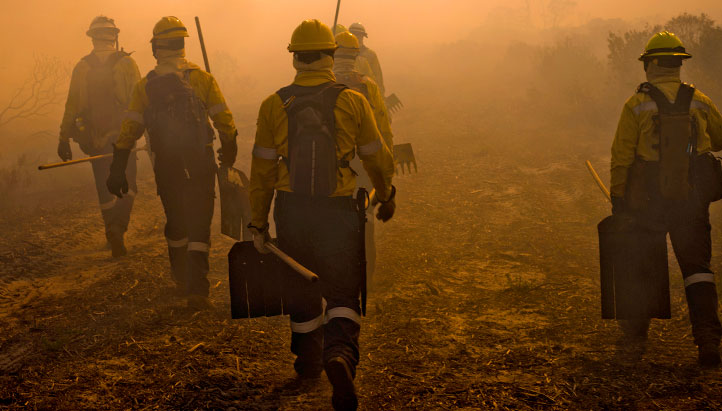 Firefighters walking surrounded by smoke with orange background