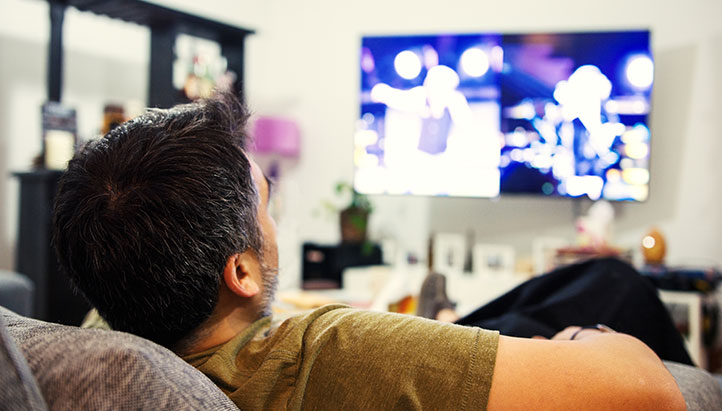 Man laying back on couch watching television