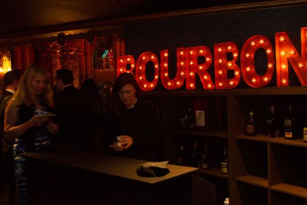 Spirit of Innovation Gala attendee at bar with lighted Bourbon sign behind the bar