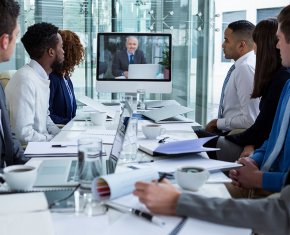 Eight professionals sitting at a table and looking at a screen with a man with a laptop