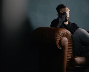 Man sitting on couch with his hand on his head as if in pain