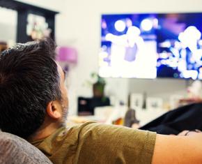 Man laying back on couch watching television